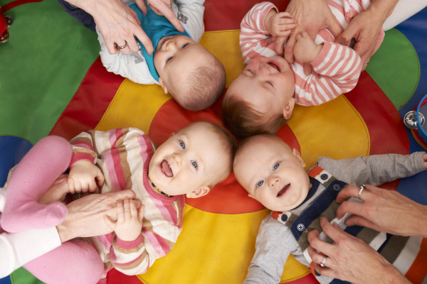 Vier Babys liegen Kopf an Kopf auf einer Krabbeldecke, werden gekitzelt und lachen.
