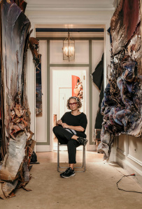 Eine Frau sitz in einem Flur, in dem überall Kunstwerke hängen.