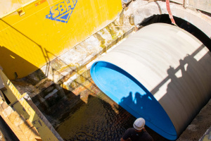 Ein großes Rohrelement wird in eine Grube heruntergelassen. Daneben steht ein Mann.