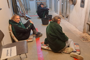 Drei Tierpfleger sitzen im Bärenhaus auf dem Boden. Ihnen gegenüber sind die Bärengehege zu sehen